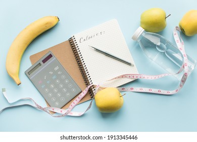 Paper notebook with word CALORIES, calculator, pen, bottle of water, measuring tape and fruits on blue background. Healthy eating concept - calculate daily nutrition intake. Top view.