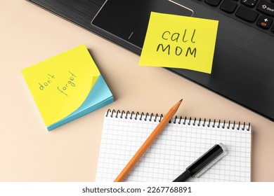 Paper notes with reminders, notebook and laptop on beige table, above view