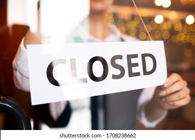 Paper with notice closed being hung by young waitress of classy restaurant or cafe standing behind the door at the end of working day - Shutterstock ID 1708238662
