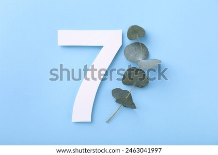 Paper number 7 and eucalyptus branch on light blue background, top view