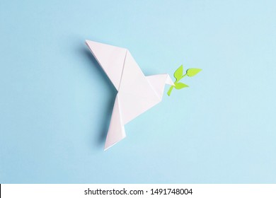 Paper origami dove of peace with olive branch on a blue background. World Peace Day concept. - Shutterstock ID 1491748004