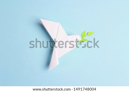 Paper origami dove of peace with olive branch on a blue background. World Peace Day concept.