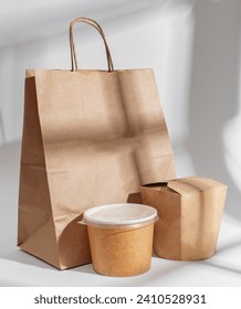 Paper package for food delivery. Beige bag, wok box and Asian soup cup in sunlight from window