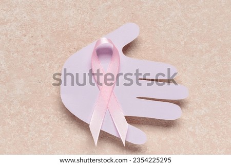 Paper palm with awareness pink ribbon on color background. Breast cancer concept