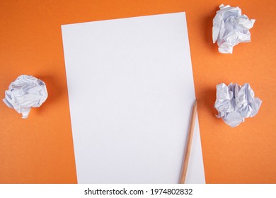 paper with pencil and wad of papers on orange background