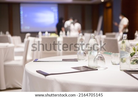 Paper, pencil, water bottle, glass on the table in the seminar room background.
