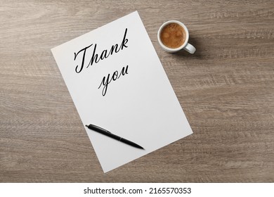 Paper with phrase Thank You, pen and cup of coffee on wooden table, flat lay