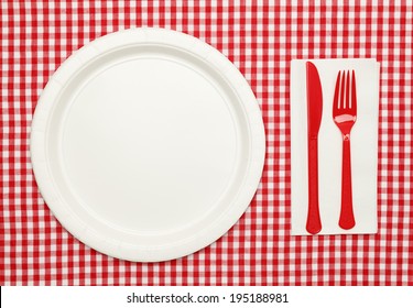 Paper Plate On Red Checkered Table Cloth With Plastic Utensils And Napkin.