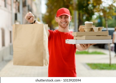 Paper Pocket And Food Containers In Hands Of A Smiling Deliveryman Outdoors. Quality Service Of A Restaurant.