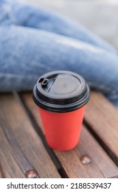 Paper red cup with black plastic lid. A cup made of eco-friendly material. Behind the cup is a jeans texture background. Gray tile texture background. Cup of coffee on a braun bench in the city. - Shutterstock ID 2188539437