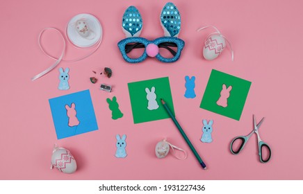 Paper, Scissors, Glasses, Eggs, Pencil, Tape And A Rabbit On A Pink Background, Top View Close-up.