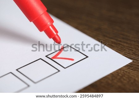 Paper sheet with checkboxes and red marker at wooden table, closeup