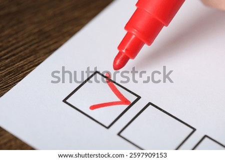 Paper sheet with checkboxes and red marker at wooden table, closeup