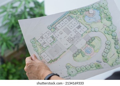 Paper Sheet Of Layout Plan With Hands And Garden Background, That Shown Design Of House Landscape Or Garden Design   Drawing By Hand With Color Marker Pens And Color Pencil, Selective Focus