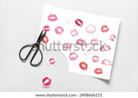 Paper sheet with lipstick kiss marks and scissors on grey background. Valentine's Day celebration