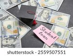 Paper sheet with text STUDENT LOAN, dollar banknotes and small graduation hat on dark background