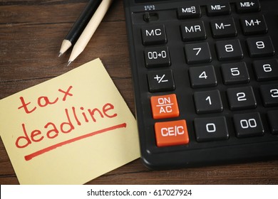 Paper sheet with text TAX DEADLINE, calculator and pencils on wooden table - Shutterstock ID 617027924