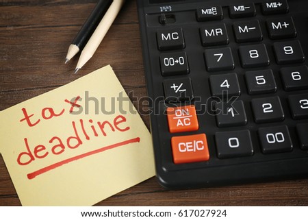 Paper sheet with text TAX DEADLINE, calculator and pencils on wooden table