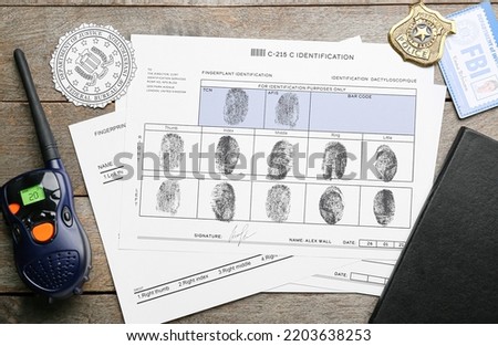 Paper sheets with finger prints, FBI seal, badge with portable radio transmitter on wooden background