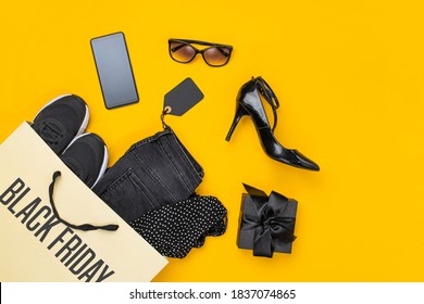 Paper shopping bag with clothes spill out on yellow background. Black friday concept. Top view, flat lay 