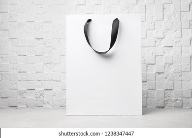 Paper shopping bag with ribbon handles on table near white wall. Mockup for design