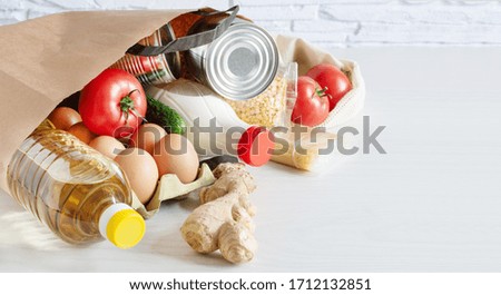 Paper shopping bag with various food. Food donation, safe delivery service concept. Pasta, eggs, canned food, bottle of oil and milk in a grocery shopping bag.