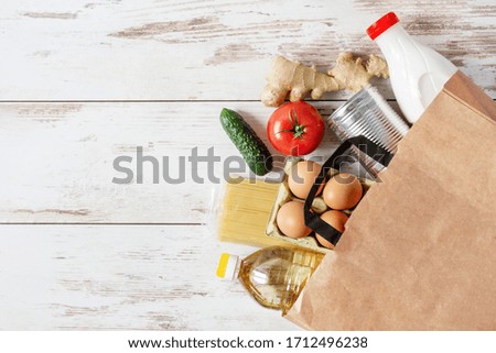 Paper shopping bag with various food. Food donation, safe delivery service concept. Pasta, eggs, canned food, bottle of oil and milk in a grocery shopping bag.