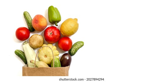 A paper shopping bag with vegetables and fruits, tomato, cucumber, squash, pepper, lemon, eggplant, zucchini, banana, apple, peach on white background - Shutterstock ID 2027894294