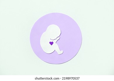Paper silhouette of a human embryo with a heart in a purple circle on a white background. Flat lay, place for text.