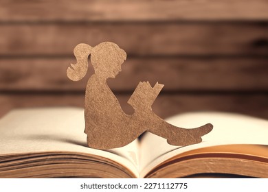 Silhouette de papel de una niña leyendo un libro sobre un fondo de madera. Día mundial del libro y de los derechos de autor. Día Internacional del Conocimiento. día mundial de la salud mental