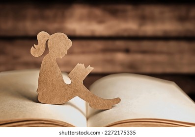 Silhouette de papel de una niña leyendo un libro sobre un fondo de madera. Día mundial del libro y de los derechos de autor. Día Internacional del Conocimiento. espacio de copia