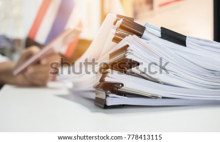 Paper stack, Pile of unfinished documents on office desk related to business functions. Stack of business papers for Annual Report files on blur National flag,use smart phone. Business offices concept