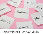 Paper stickers with different names on pink background, closeup. Choosing baby