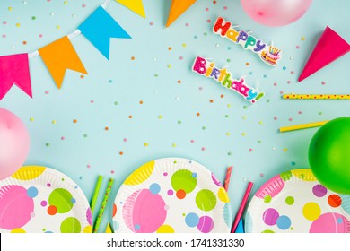 Paper Tableware For A Holiday. Birthday Party Decoration On A Blue Background. Frame Or Background With Colorful Plates, A Carnival Cap And Streamers. Eco-friendly Food Items.