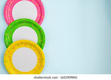 Paper Tableware For A Holiday On A Blue Background. Yellow, Green, And Pink Plates, Tubes, And Glasses. The Concept Of Holiday Cookware For A Picnic .Eco-friendly Food Items.