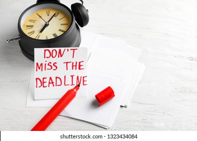 Paper with text DONT MISS THE DEADLINE and alarm clock on white wooden table