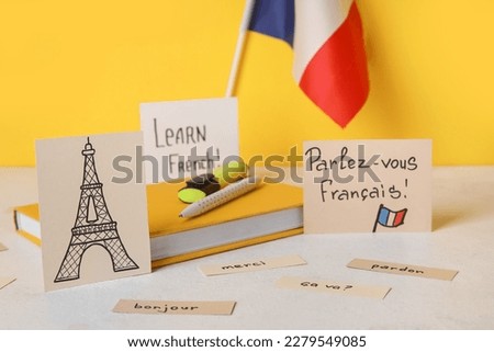 Paper with text LEARN FRENCH, drawn Eiffel Tower, flag and stationery on table near yellow wall