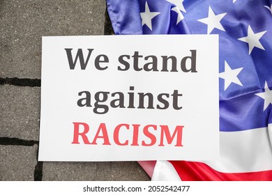 Paper With Text WE STAND AGAINST RACISM And Flag Of USA Outdoors