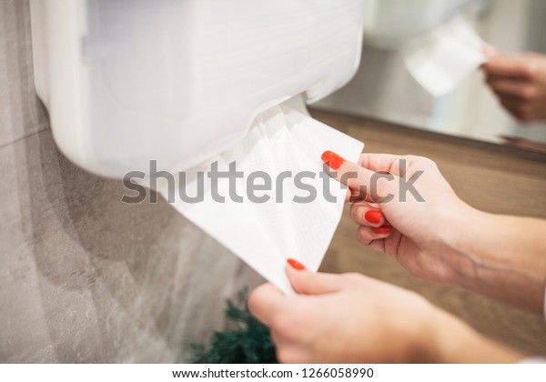 Paper towel dispenser. Hand of woman takes\
paper towel in bathroom.