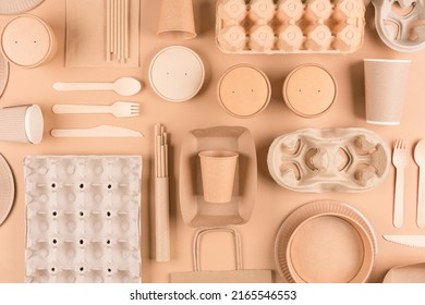  Paper utensils and tableware, wooden cutlery set, paper cups, plates, bags, pulp egg boxes and food containers over light brown background. Top view. Sustainable food packaging concept