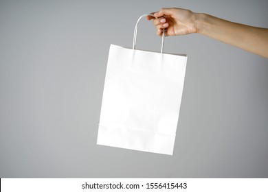 Paper White Craft Bag, Eco Packaging In A Female Hand, On A Gray Background, With Place For Text.