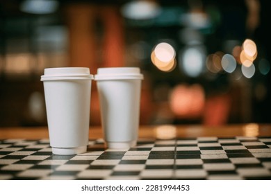 Paper white cups of tea or coffee are taken out on the coffee shop table. No one. Two glasses are standing on the bar counter of the cafe against the background of glare. Place for the inscription.