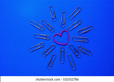 Paperclip On A Blue Background In The Center Of The Pink Clip In The Shape Of A Heart