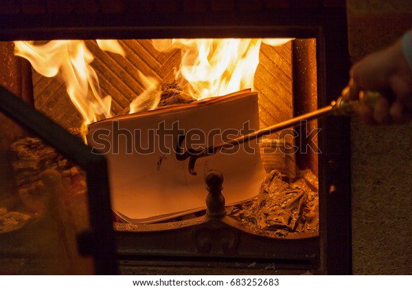 papers in the fire.\
Sheets of paper burning in a fireplace flames. Their presses brass\
poker with a hook\
