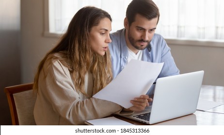 Paperwork At Home Office. Pensive Concentrated Millennial Family Couple Sitting By Laptop Studying Paper Bills Discussing Terms Conditions Of Loan Mortgage Agreement Preparing To Make Payment Online