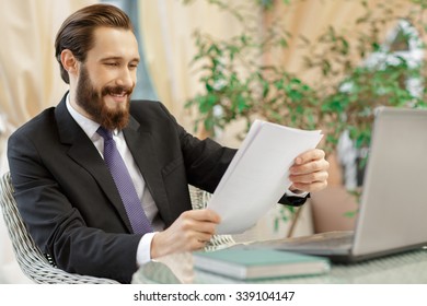 Paperwork Is Not That Boring. Bearded Smiling Businessman Checking Papers Over Lunch In The Restaurant