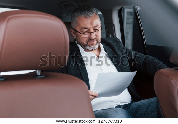 Paperwork on the back seat of the car. Senior\
businessman with\
documents.