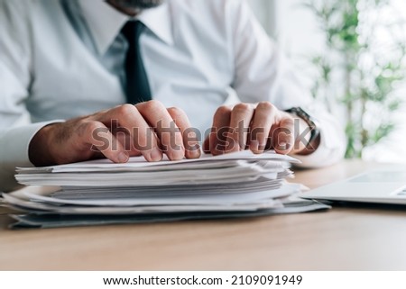 Paperwork workload, businessman with stack of reports for reviewing on office desk, selective focus