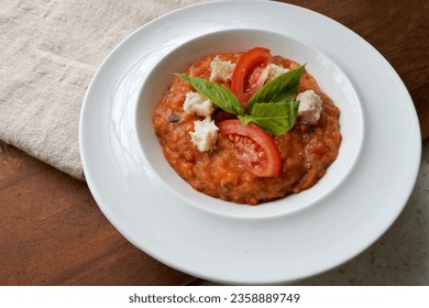 Pappa al Pomodoro, traditional italian tuscan dish, soup with tomatoes and bread. In a white plate. Homemade. Wood background.