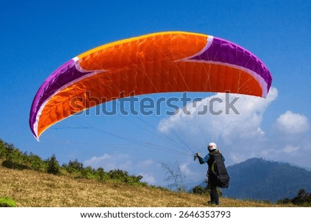 A para glider sets up for flight, positioning their colorful fabric against a backdrop of mountains and clear skies.